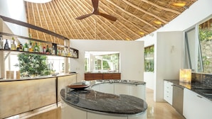 A modern kitchen with a curved island, a bamboo ceiling, and a view of greenery outside.