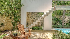 A modern outdoor area with a stone wall, wooden chairs, a concrete staircase, and a pool.