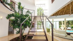 A modern interior with a central staircase, indoor plants, and a view of an outdoor area with a pool.