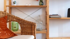 Ein Korbstuhl mit braunem Kissen und weißem Kopfkissen, eine grüne Vase und eine klare Glasflasche auf einem Holzregal.