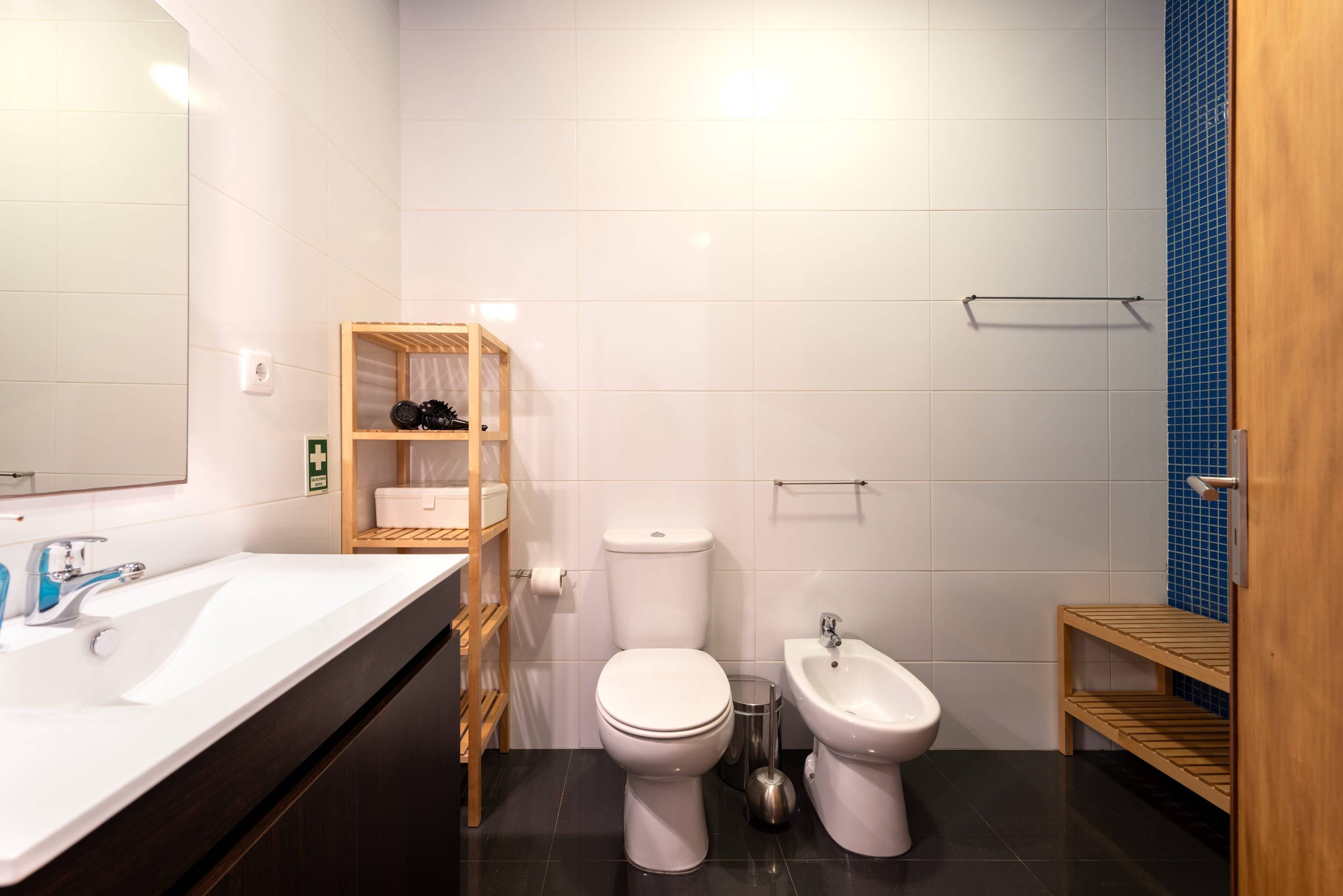 Ein modernes Badezimmer mit Waschbecken, Toilette, Bidet und Holzregalen.