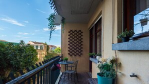 Ein Balkon mit Holzboden, einem kleinen runden Tisch mit Stühlen, Blumentöpfen und einer Rankgitterwand.