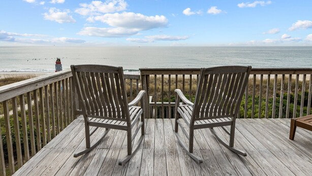 A wooden deck with two rocking chairs facing a beach.