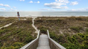 A wooden boardwalk leading to a beach with a signpost in the distance.