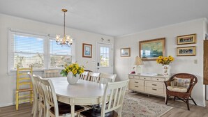 A dining area with a round table, white chairs, a chandelier, and a vase of yellow flowers.