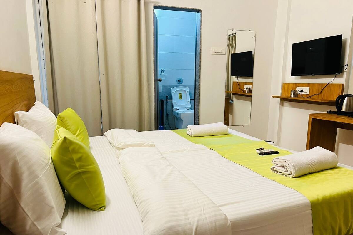 Une chambre d’hôtel avec un lit, des oreillers, une télévision, un miroir et une petite table avec une bouilloire.