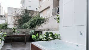 Una terraza en la azotea con una mesa de madera, plantas en macetas y un jacuzzi.