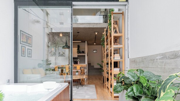 Un interior moderno con una puerta de vidrio que da a una sala de estar, una escalera de madera y un estante empotrado para plantas.