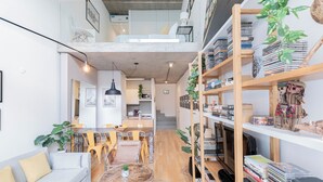 Un espacio habitable moderno con comedor, sofá, mesa de centro y una estantería llena de libros y objetos decorativos.