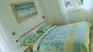 A bedroom with a bed, a painting of the sea, and a window with curtains. - Charming studio with balcony, WiFifree parking and AC in adorable old town Brseč (Brsec)