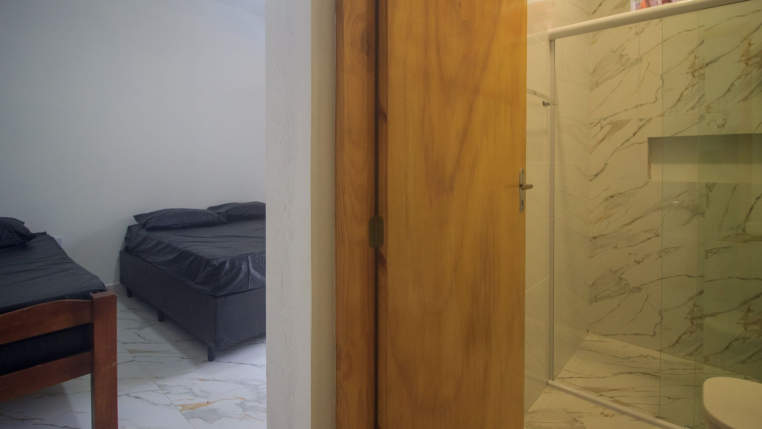 Una habitación con dos camas, una puerta de madera y un baño con baldosas de mármol.