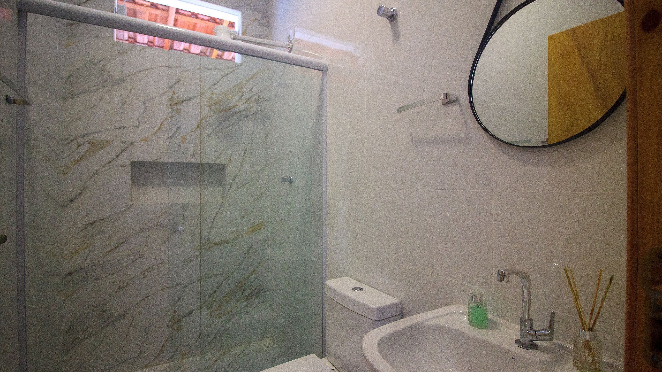 A bathroom with a marble shower enclosure, a toilet, a sink with a mirror, and a small bottle of soap.