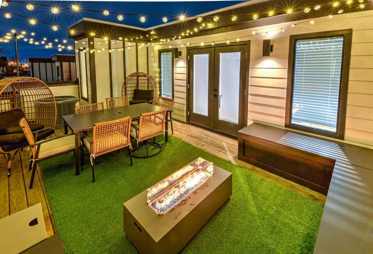 An outdoor patio with a table and chairs, a fire feature, and string lights.