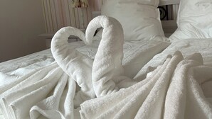 Una cama con dos toallas con forma de cisnes, un muro a rayas y un sombrero en la pared.