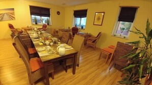 Un comedor con una larga mesa de madera dispuesta para una comida, rodeado de sillas de mimbre y una planta en maceta.