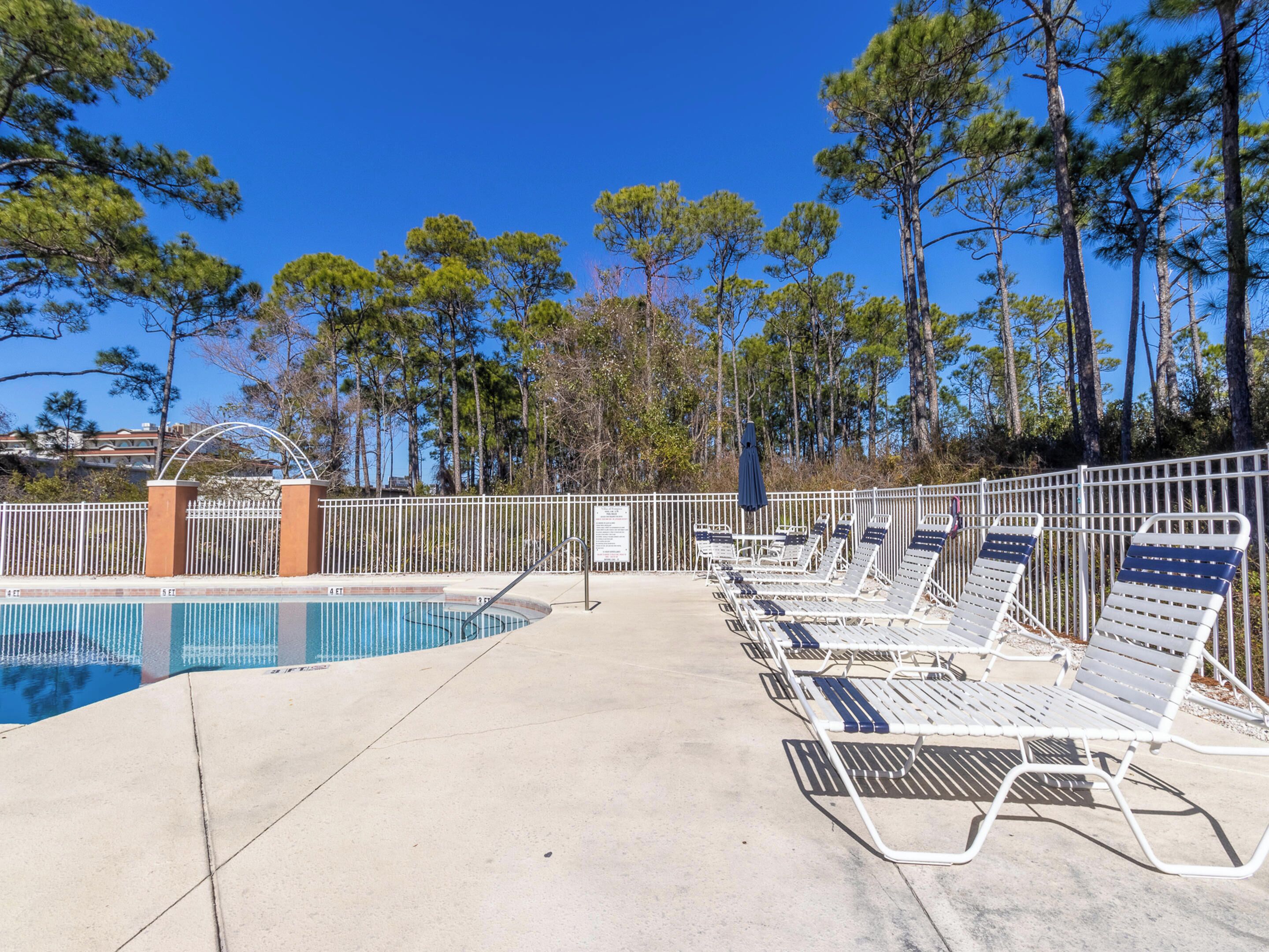 A pool area with lounge chairs and a fence.