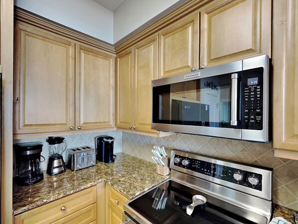 A kitchen with wooden cabinets, a built-in microwave, a stovetop oven, and a coffee maker. - Azure #511 | Gulf Front, Central Location, Resort Amenities (Fort Walton Beach)