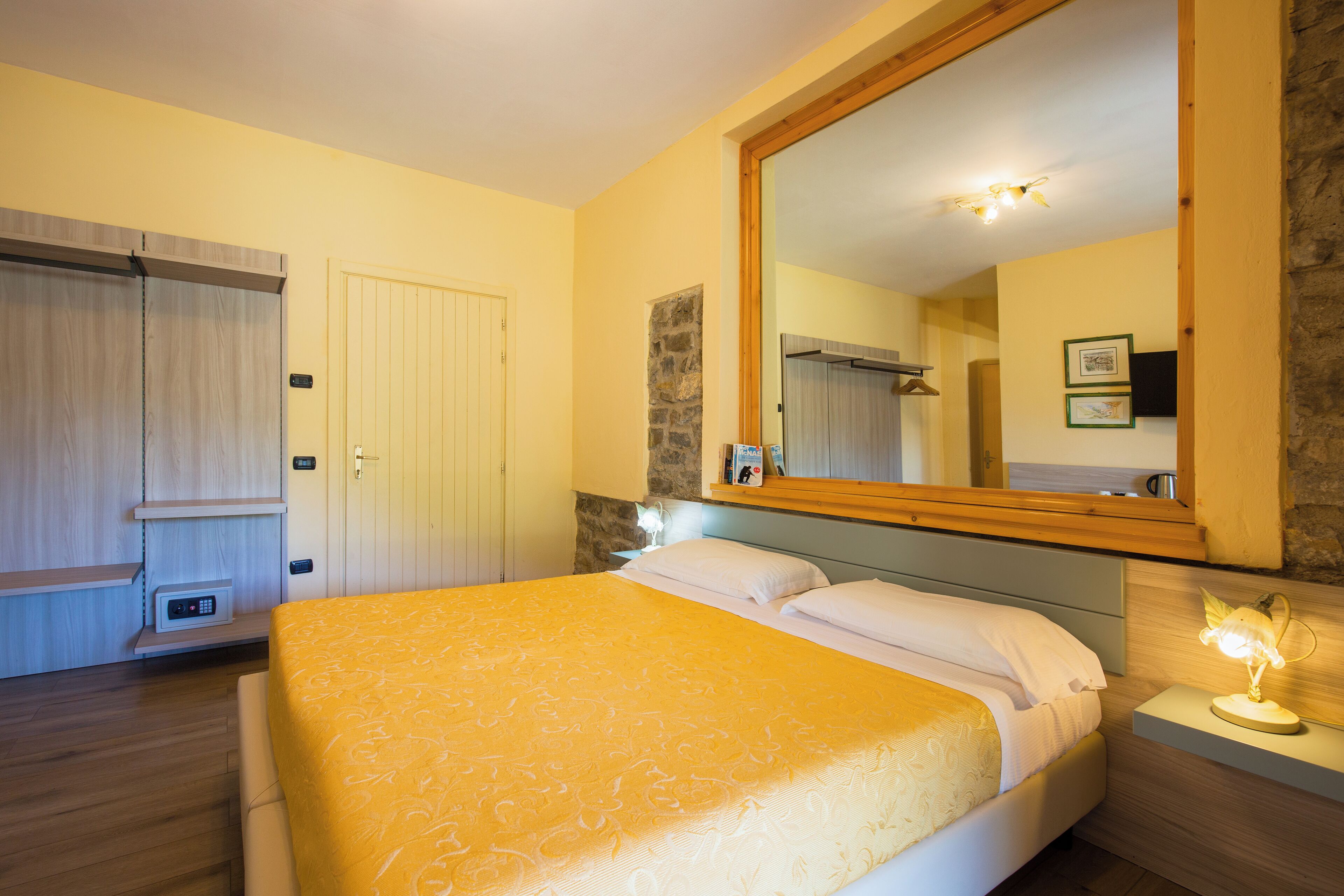 A bedroom with a bed, a nightstand, a mirror, a wardrobe, and a small table with a lamp.