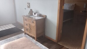 Een slaapkamer met een bed, een houten dressoir, een flatscreen televisie aan de wand en een schuifdeur die naar een andere kamer leidt.