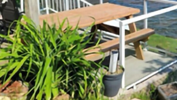 Een terras met een houten tafel en stoelen met uitzicht op een meer, omringd door groen.