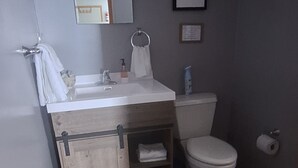Een badkamer met een houten wastafel, toilet, wastafel met spiegel en douche.