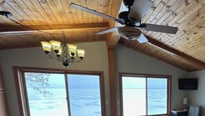 Een ruime woonkamer met grote ramen met uitzicht op zee, een plafondventilator en een kroonluchter.
