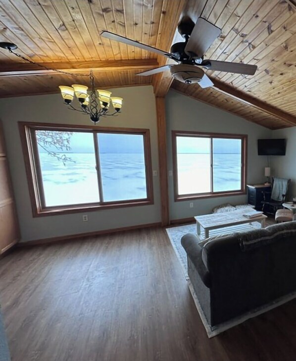 A spacious living room with large windows overlooking the sea, a ceiling fan, and a chandelier. - Leech lake cabin with gorgeous views!  2br/2ba pet friendly! 6 PERSON HOT TUB! (Walker)