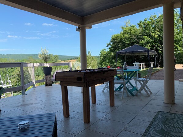 A covered patio area with a foosball table, outdoor seating, and a view of the landscape.