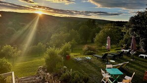 A garden with a table and chairs, a stone wall, and a view of the sunset over a hilly landscape. - Gite "La maison de la colline" 5 minutes de Tournus Sud Bourgogne (Vers)
