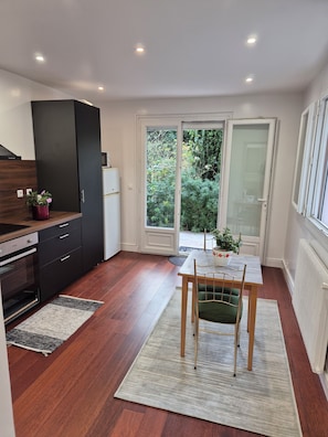 A modern kitchen with dark cabinetry, a built-in oven, and a dining area with a table and chairs.