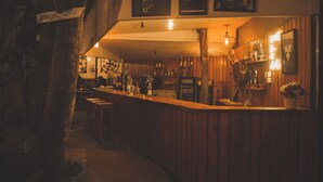 A dimly lit bar with wooden paneling, a counter with various bottles, and framed pictures on the wall. - Gypsy hostel & Backpackers (Pokhara)