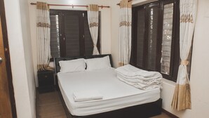 A neatly made bed with white linens, a wooden headboard, and a window with curtains. - Gypsy hostel & Backpackers (Pokhara)
