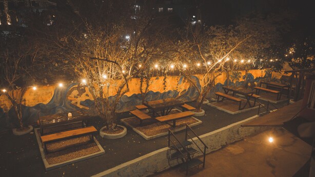 An outdoor seating area with benches and tables, surrounded by trees and illuminated by string lights. - Gypsy hostel & Backpackers (Pokhara)