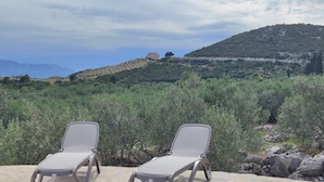 A pool area with two lounge chairs and a view of a hilly landscape with a house in the distance.