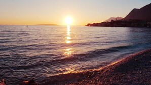 A sunset over a calm sea with a rocky shoreline and distant mountains.