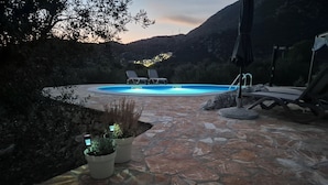 An outdoor pool area with stone flooring, lounge chairs, and potted plants.