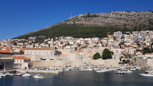 A coastal town with historic buildings, a harbor with boats, and a hill with a tower.