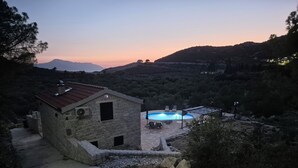 A stone house with a swimming pool, surrounded by hills and trees.