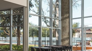 Un vaste espace intérieur doté de grandes fenêtres, d’un pilier en béton et de plusieurs tables et chaises.
