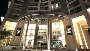 Un immeuble de grande hauteur, doté d’une entrée incurvée et agrémenté d’un élément décoratif aquatique à l’avant.