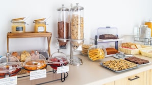 A buffet with various food items, including jars of spreads, bowls of fruit, and trays of baked goods.