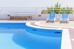 A swimming pool with two lounge chairs, a stone bench, and a white railing.