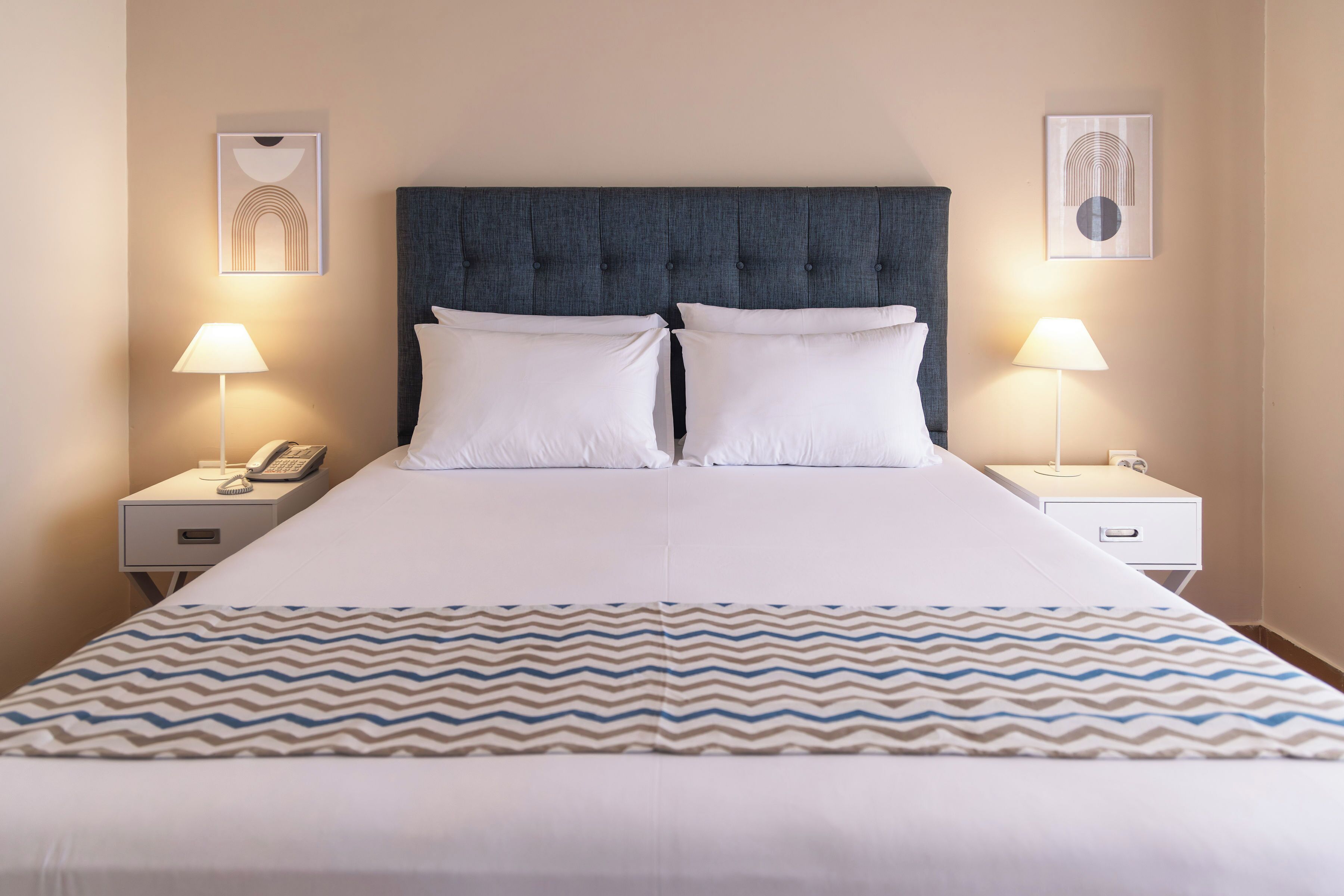 A neatly made bed with a patterned bedspread, two bedside lamps, and a phone on the nightstand.