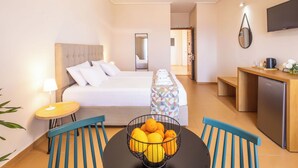 A hotel room with a bed, a dining table with chairs, a kitchen area, and a TV mounted on the wall.