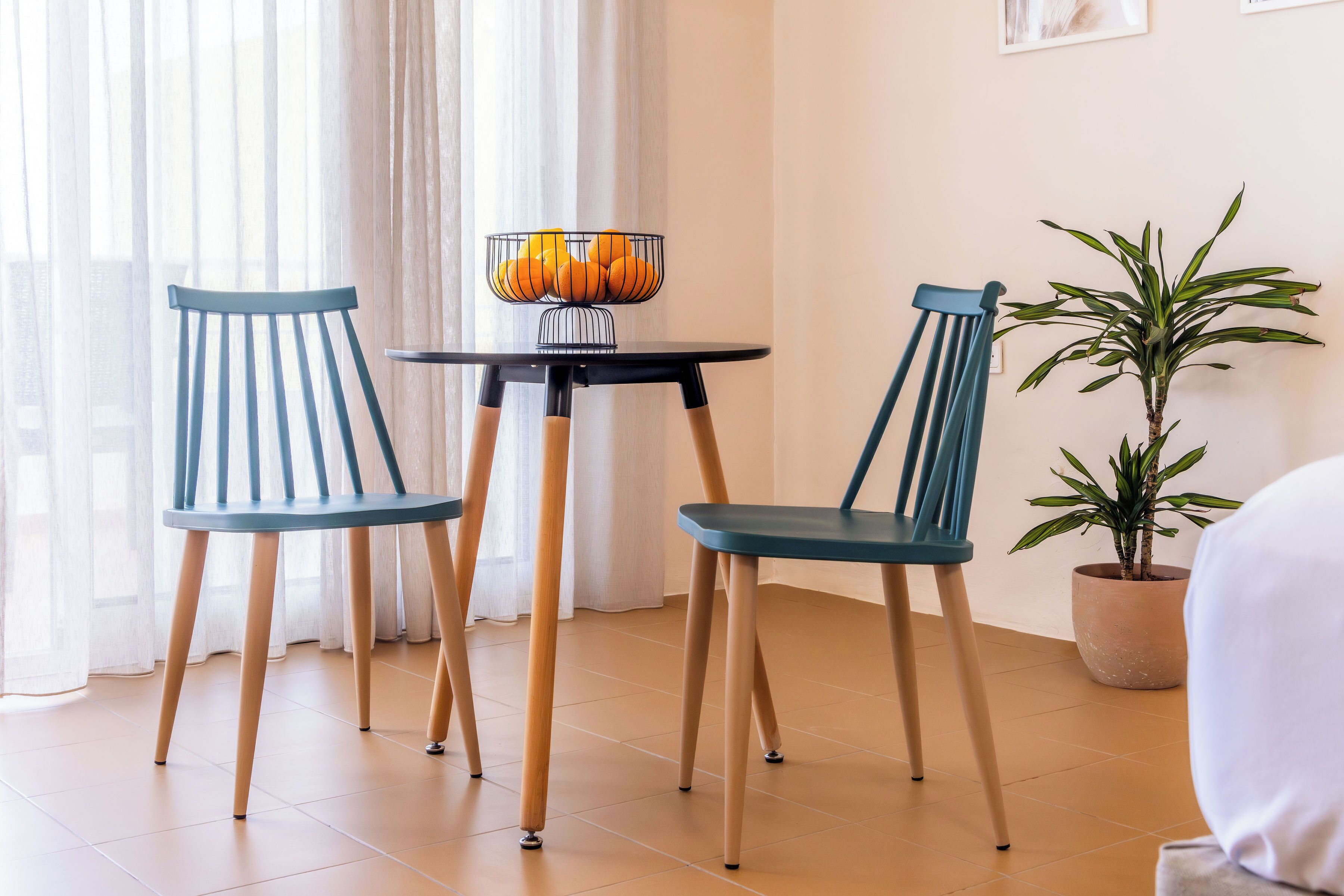 Une pièce avec deux chaises, une petite table sur laquelle se trouve un panier de fruits, une plante en pot et un lit.