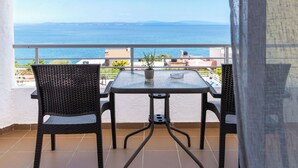 A balcony with a table and chairs, a potted plant, and a view of the sea.