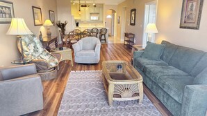 A living room with a sofa, armchairs, a coffee table, and a dining area with chairs and a table.