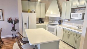 A modern kitchen with white cabinets, a central island, and a dining area with wooden chairs.