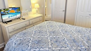 A hotel room with a bed, a dresser, a television displaying 'OCMD GETAWAYS', and a door.