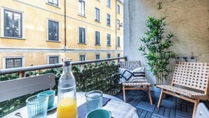 A balcony with a table set for two, two chairs, a potted plant, and a bottle of orange juice. - Elegant & Spacious 3-Bedroom Apartment in Milan’s Historic Center (Milano)